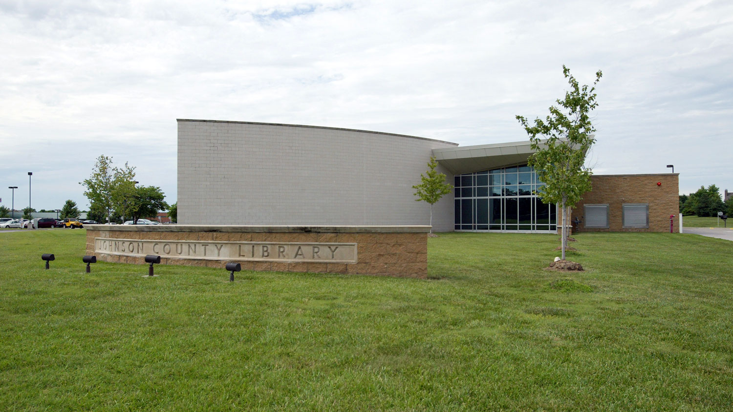 library building with brick sign in grassy lawn, curved wall, tall glass windows, and brick-faced delivery area
