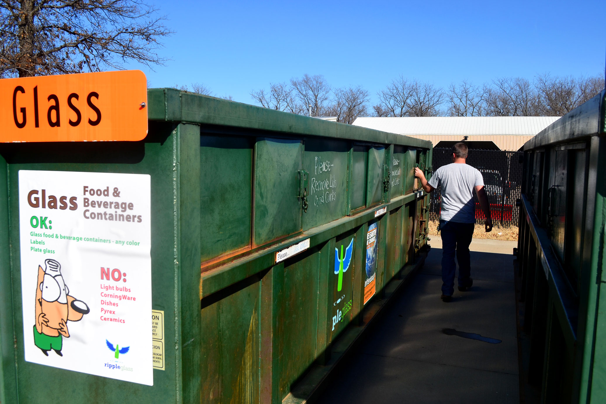 man walks between large green recycling dumpsters during winter