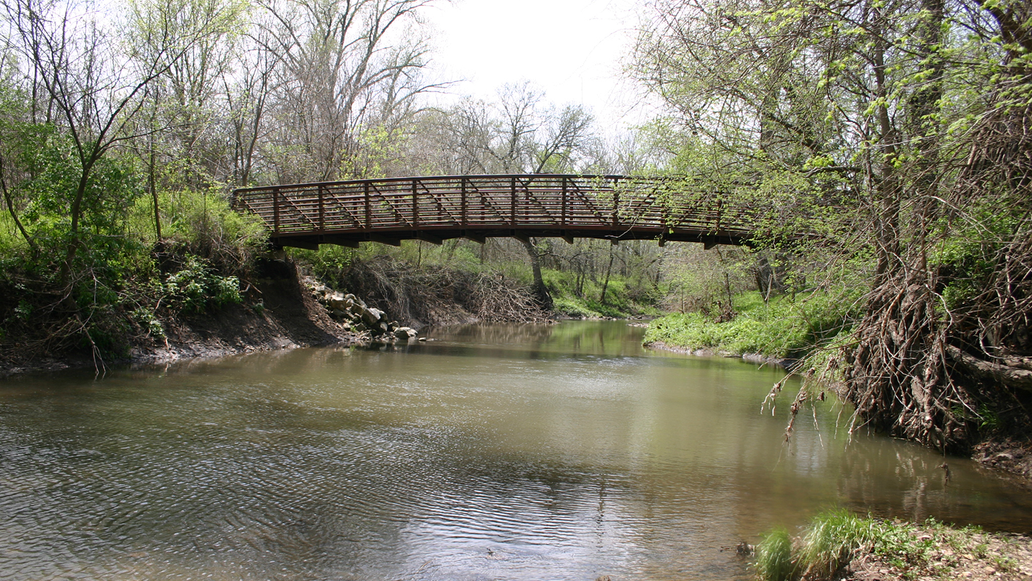 A bridge spans across a stream lined with trees at the Overland Park Arboretum & Botanical Gardens.