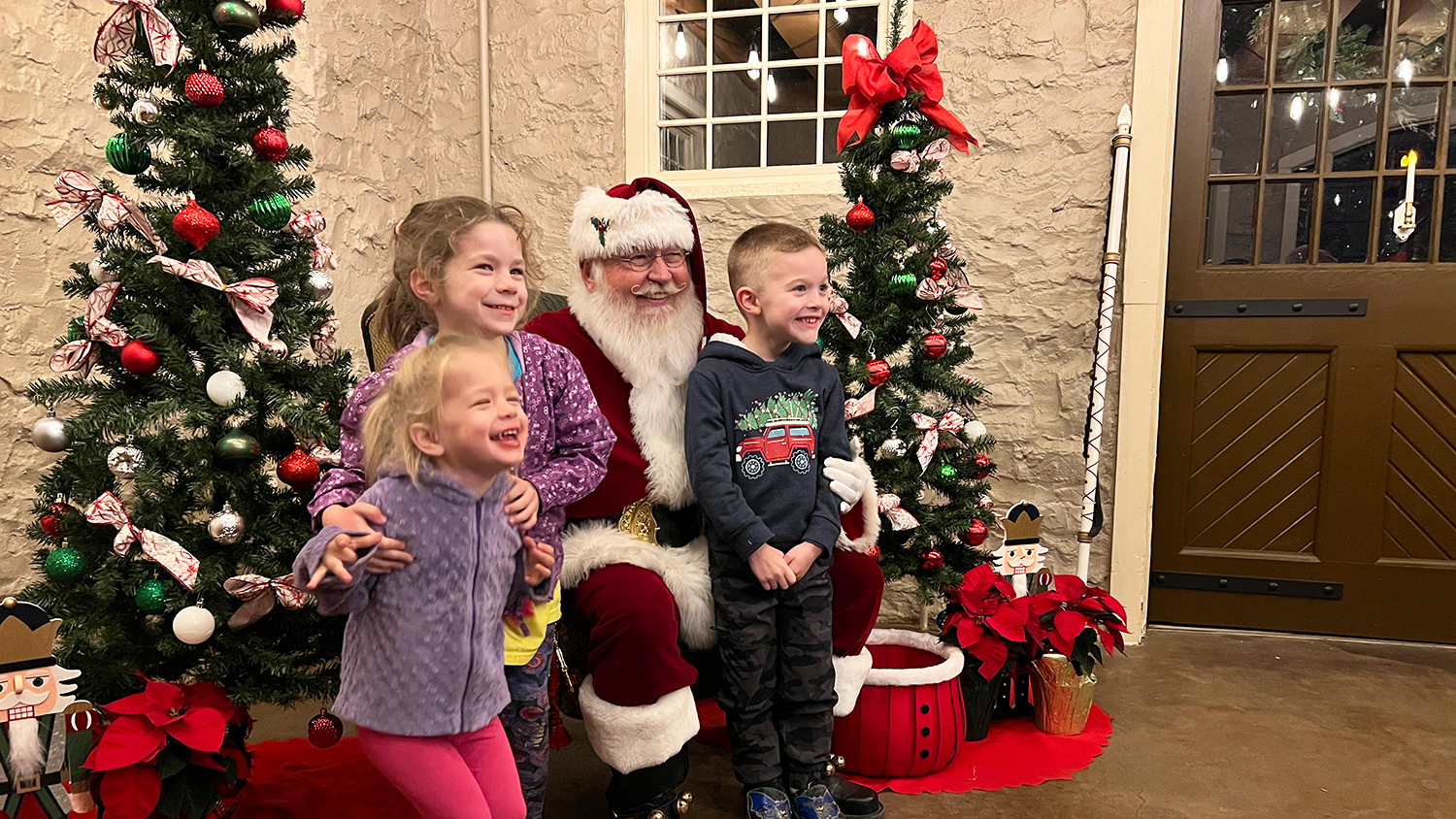 Three small children smile as they pose with Santa.