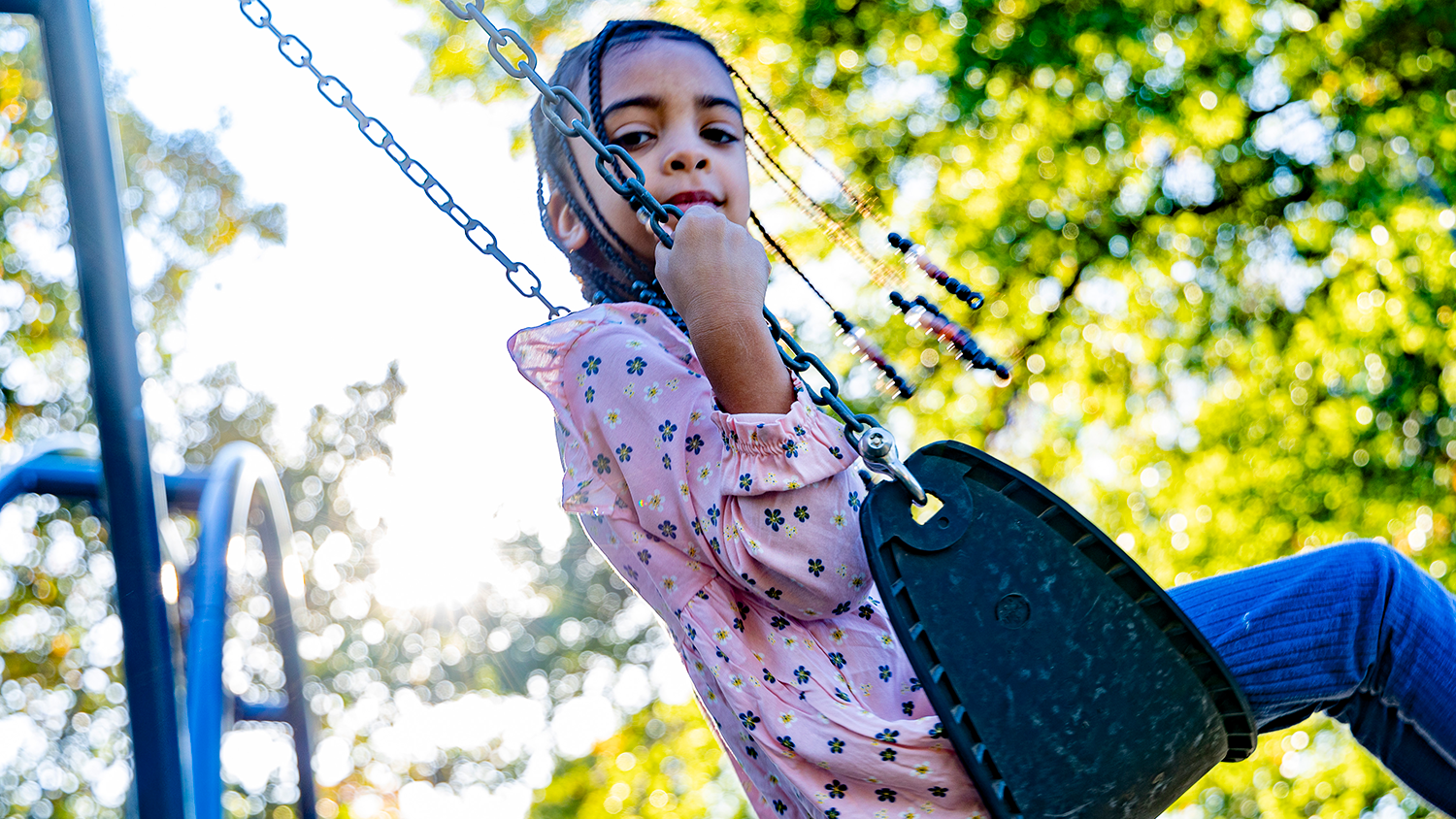A young child looks down at the camera while swinging in a city park.