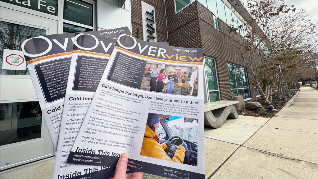 Three copies of the Winter Overview are held in front of the entrance to City Hall.
