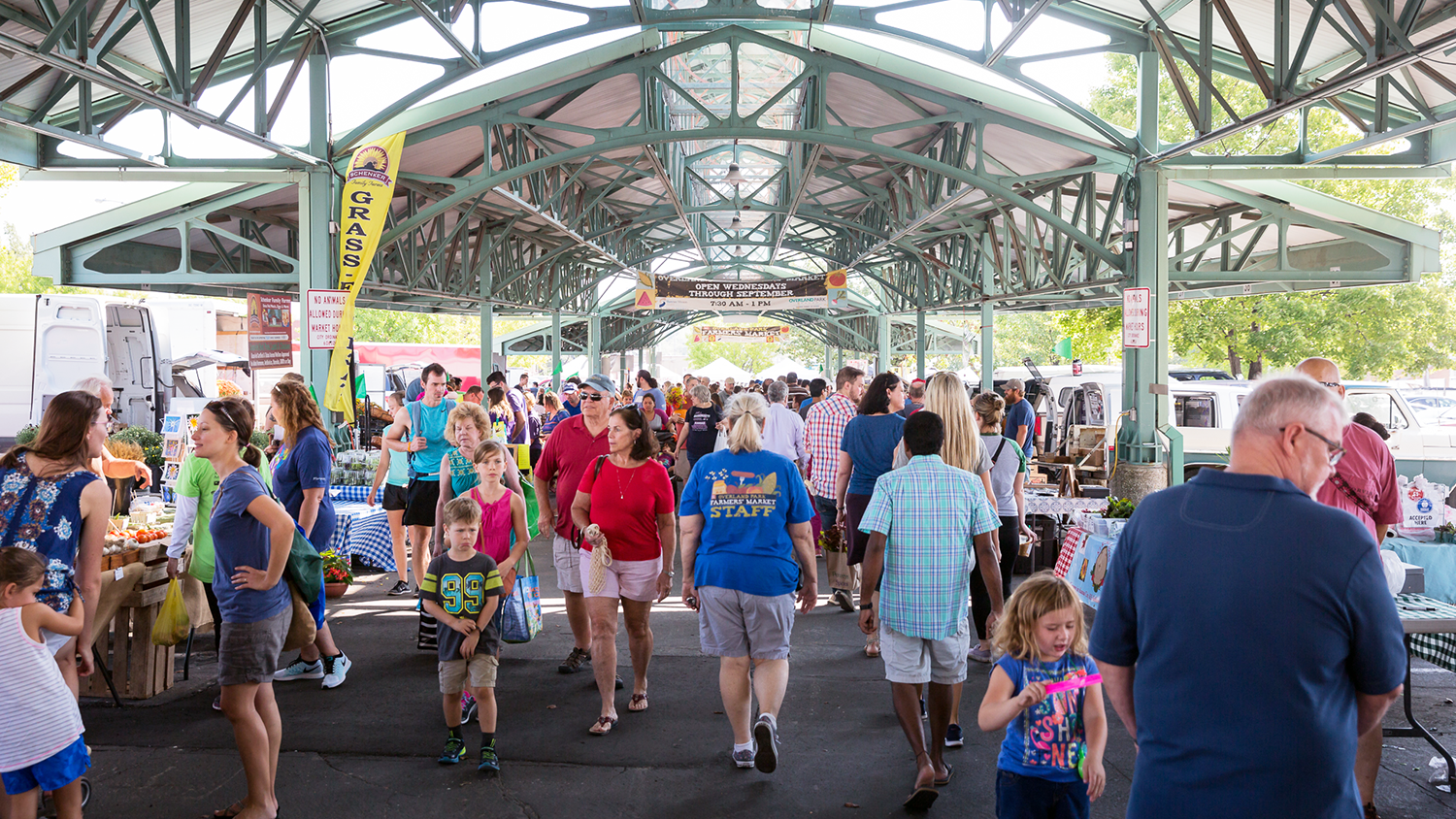 A crowd browses vendors under the Farmers' Market pavilion.