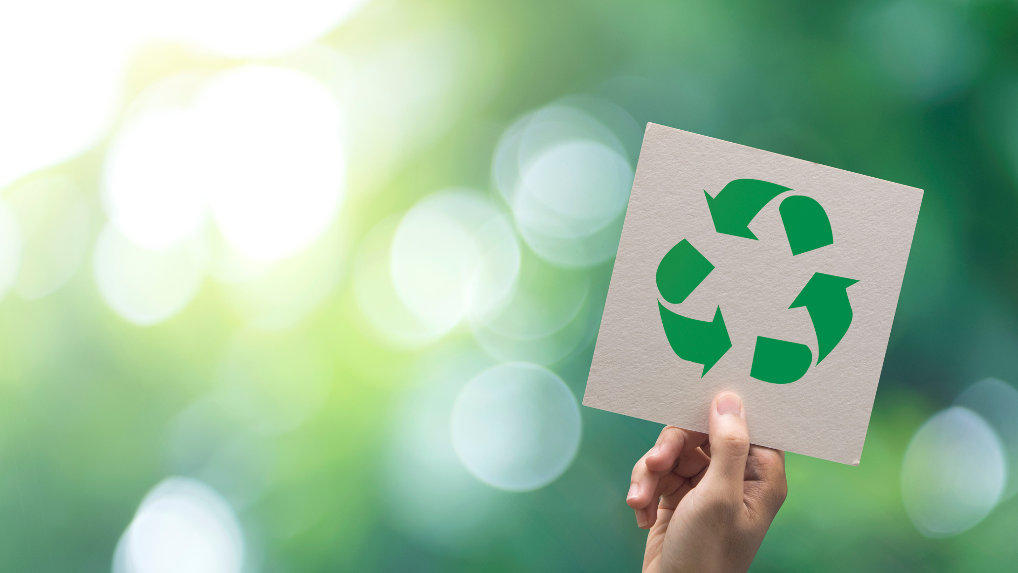 A hand holds a rectangular paper card that had a green recycle logo on it.