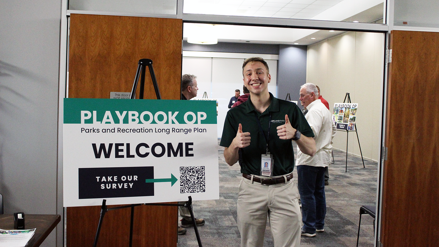 City staff member holds two thumbs up next to a Playbook OP open house sign.