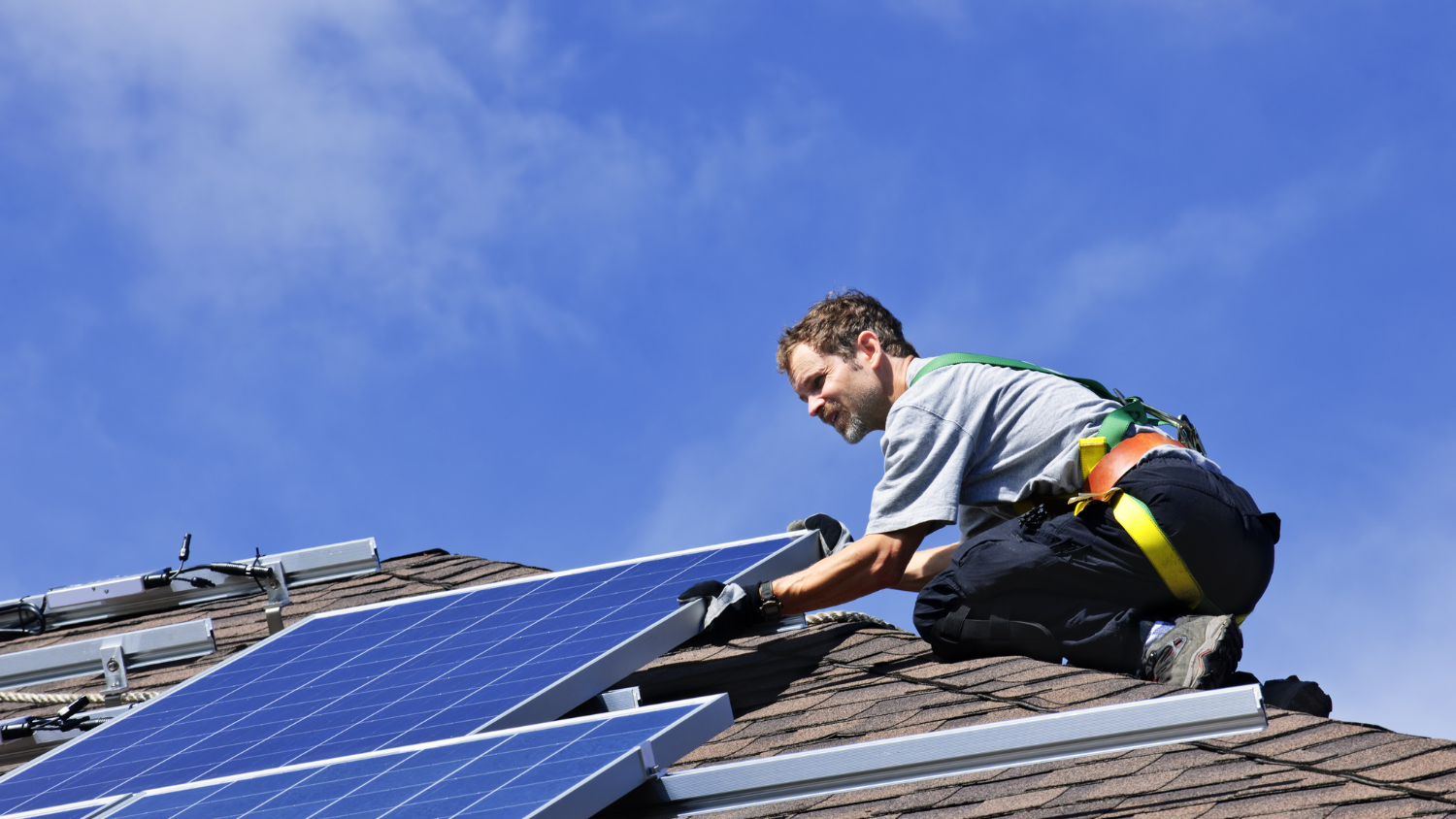 A man installs solar panels on a roof.
