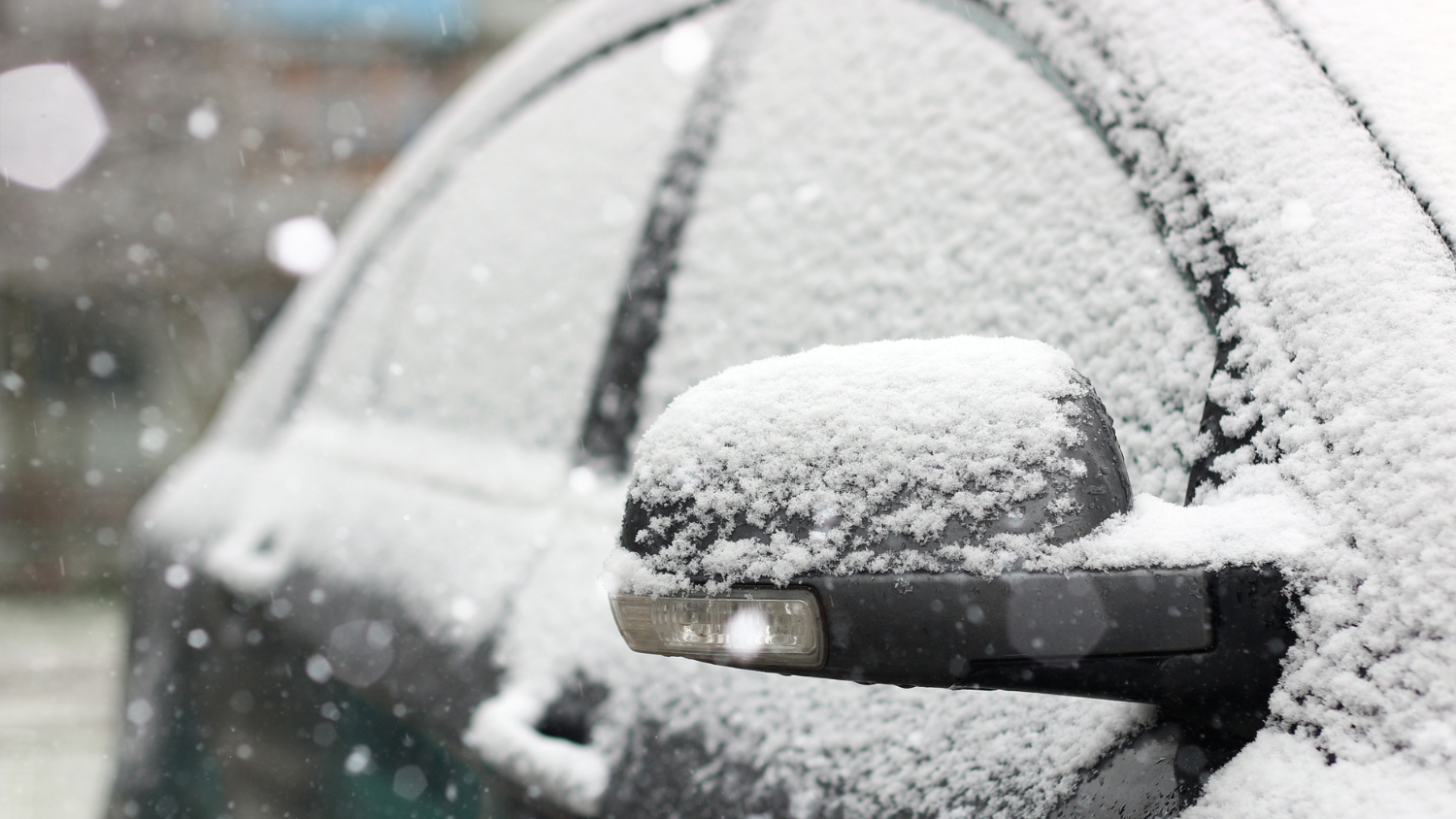 Snow begins to cover a parked vehicle.