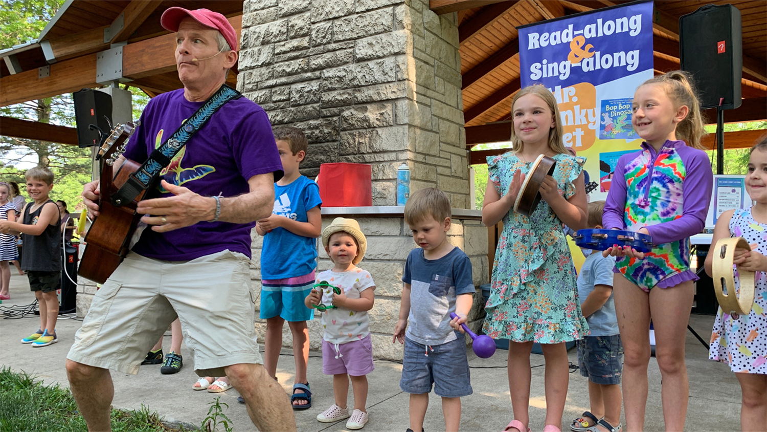 Children's performer, Mr. Stinky Feet, plays guitar while children play musical instruments behind him.