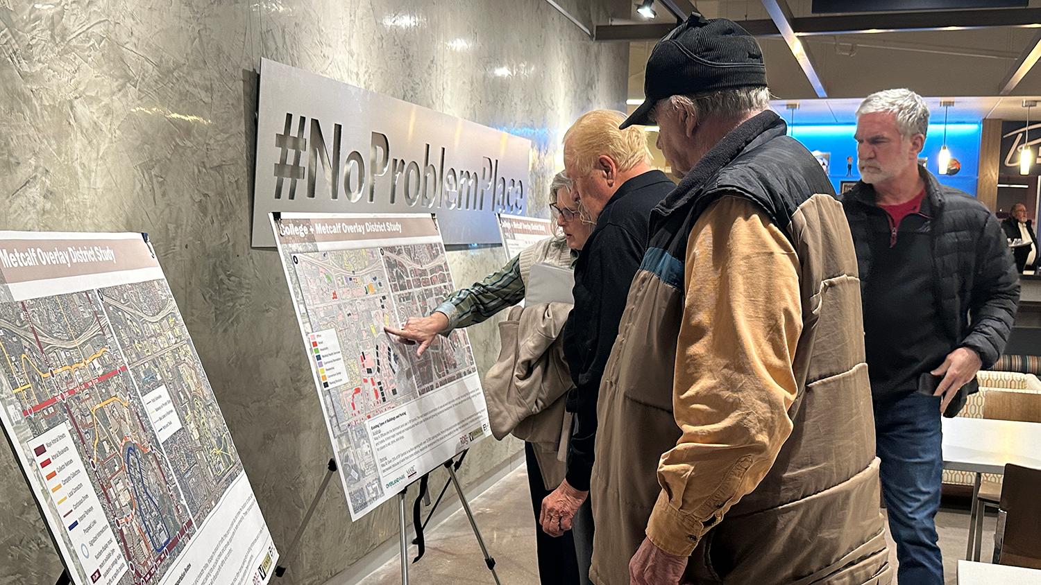 A small group of people look at information presented on a display board at a public information meeting.
