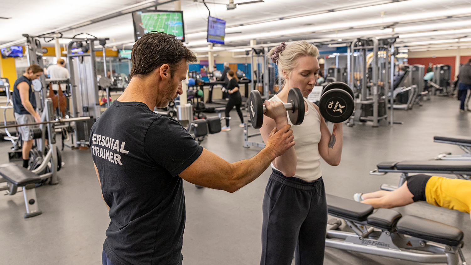 A personal trainer assists a client lifting weights at Matt Ross Community Center.