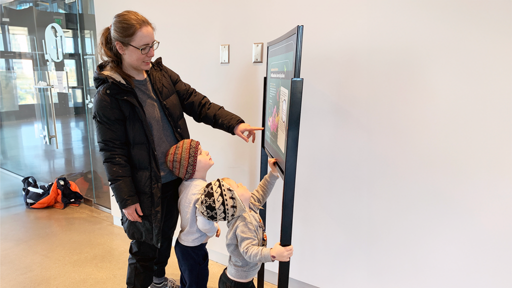 Woman and two young kids read exhibit poster at LongHouse