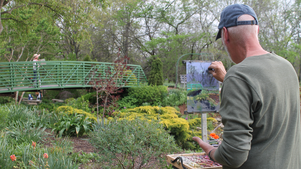A man sketches a footbridge and surrounding plants and flowers at the Overland Park Arboretum & Botanical Gardens.