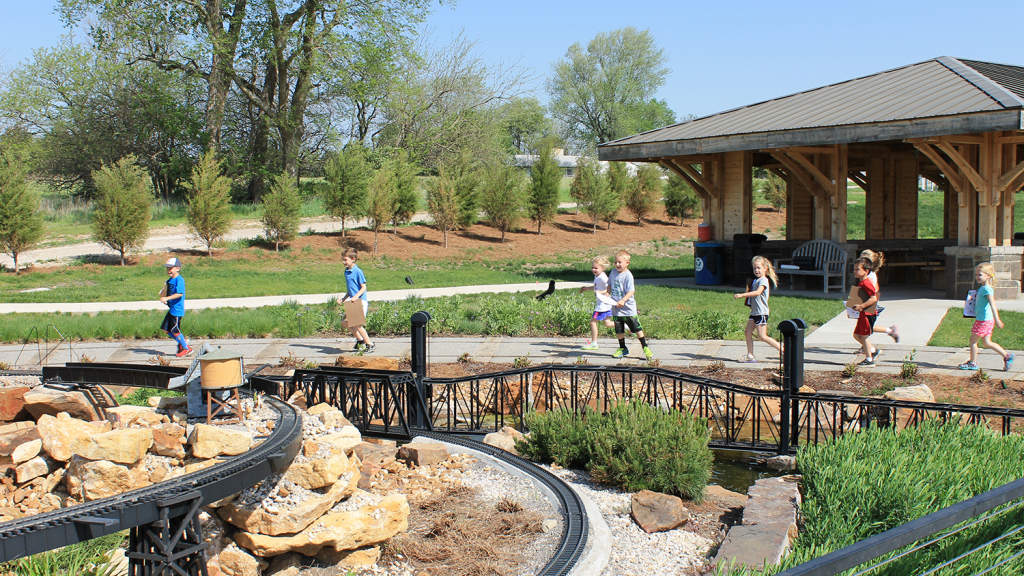 Children hold clipboards and run along a path at the arboretum.