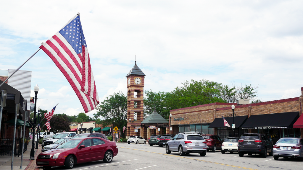 The American flag hangs near a business in Downtown Overland Park with the clocktower in the background.