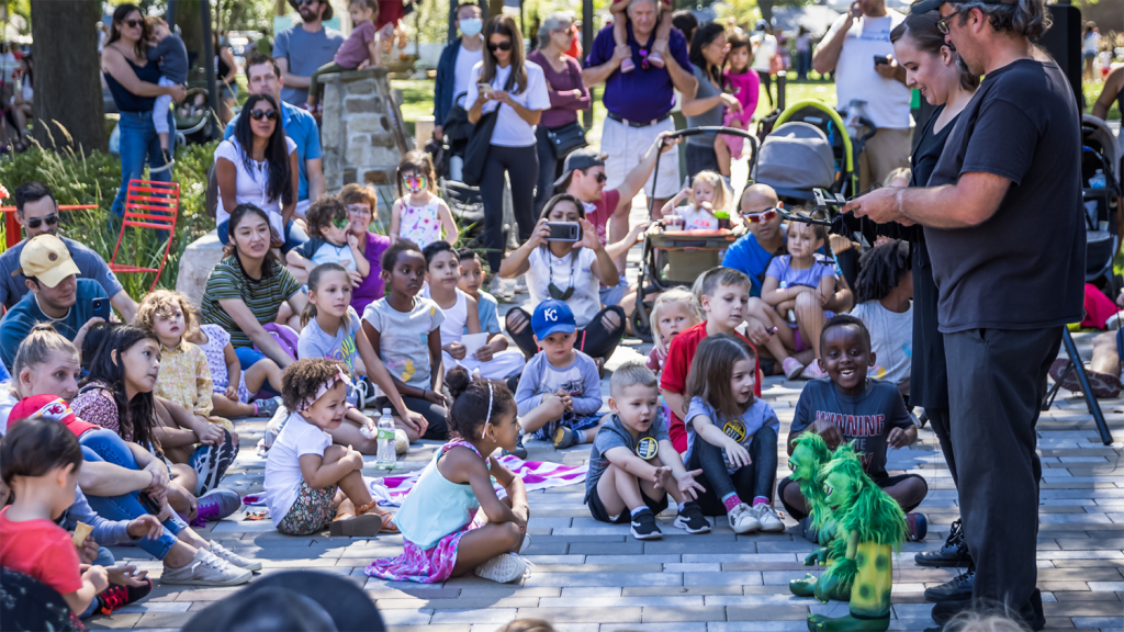 A crowd of children watch a puppet show performance.