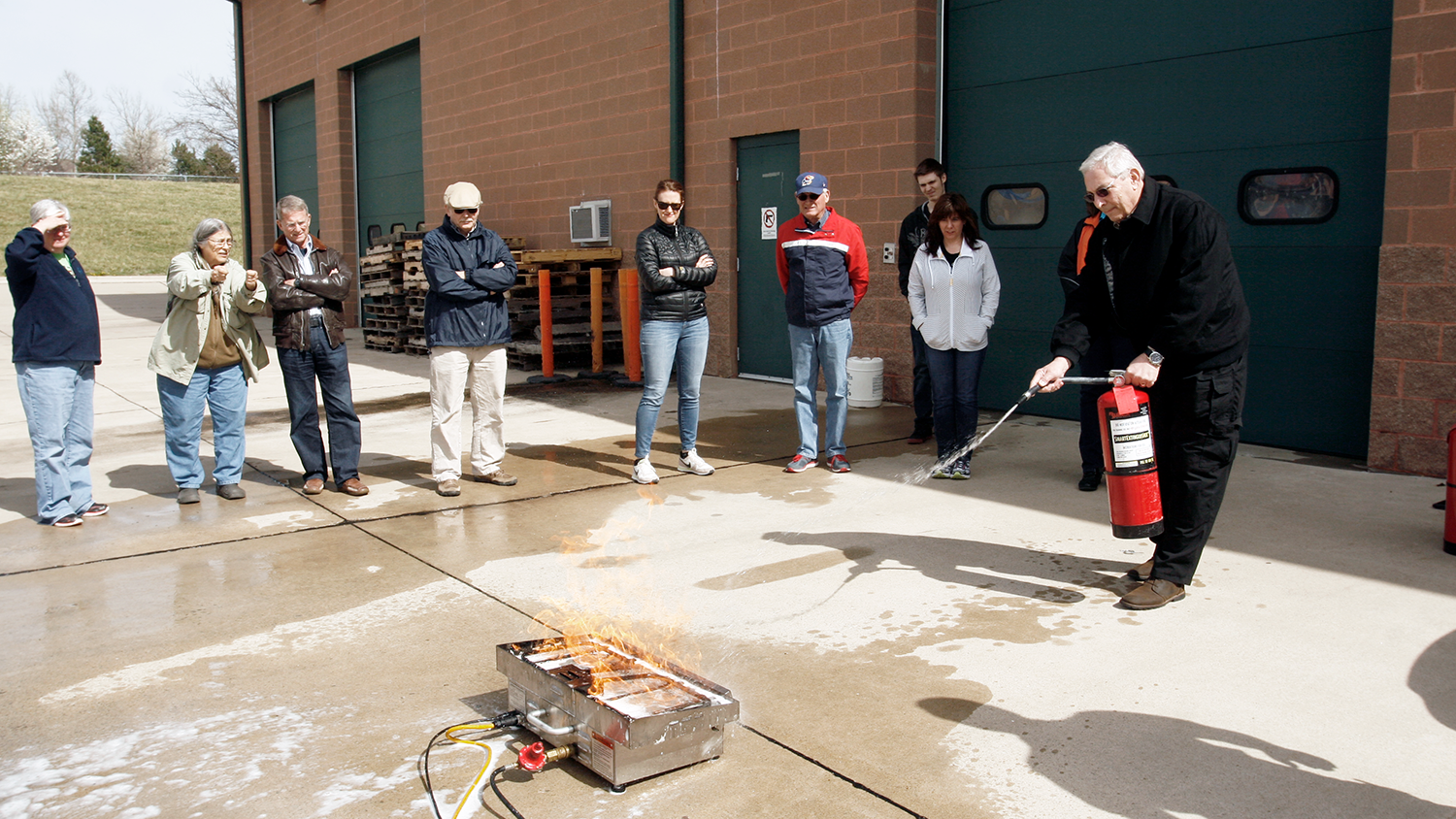 A man demonstrates putting out a controlled fire using an extinguisher.