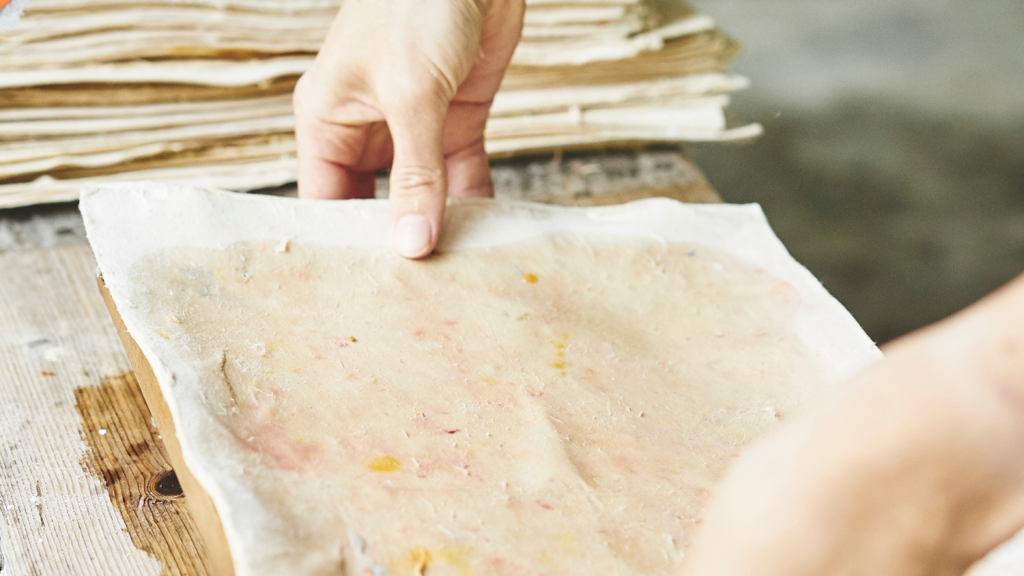 To hands lay a thick, wet piece of paper onto a table.