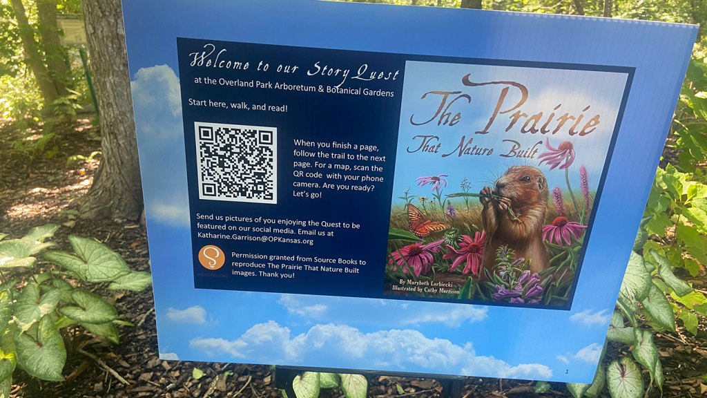 Yard sign placed in a forest at the Overland Park Arboretum & Botanical Gardens for the Walk and Read event. The sign indicates that the picture book people read on the path is titled "The Prairie that Nature Built."