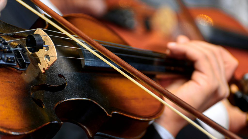 A bow slides across violin strings and a musician plays in an orchestra performance.