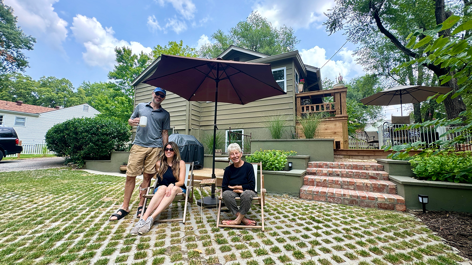 Three people sit in lawn chairs in their backyard, which has narrow, intersecting lines of concrete for stormwater run-off.