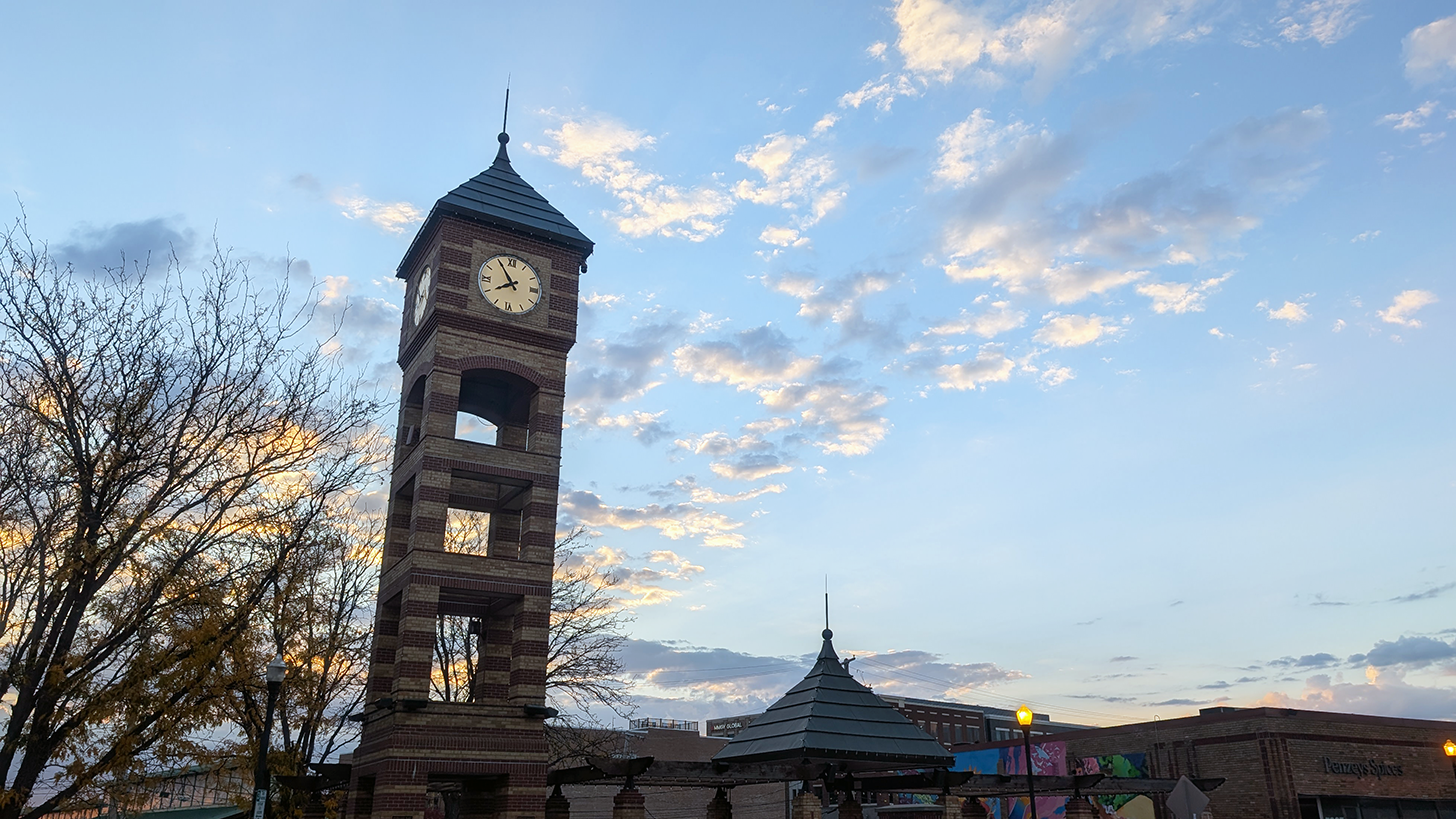 Downtown Overland Park's Clock Tower's face is illuminated as the sun sets in the distance.