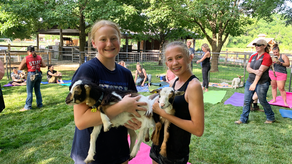 Two girls hold young goats at Goat Yoga.