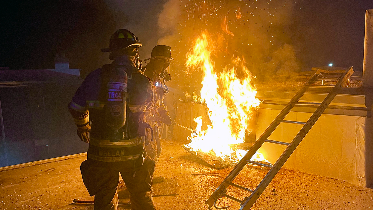 Two firefighters work to extinguish a small fire on the roof of a building.