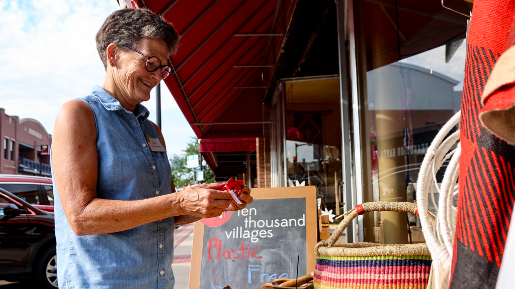 A woman smiles, holding a small figurine outside a Downtown Overland Park small business.