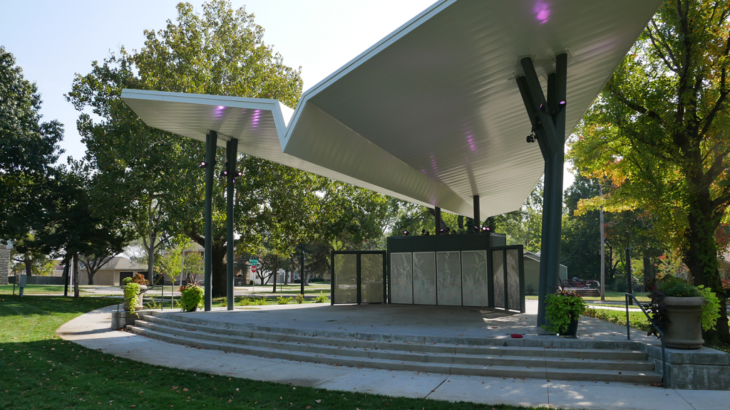 A park structure's large roof provides shade for the concrete stage underneath it.