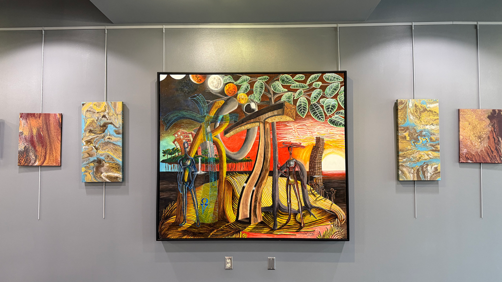 A large square painting hangs on a wall, depicting two abstract people standing on either side of a tree and cross.