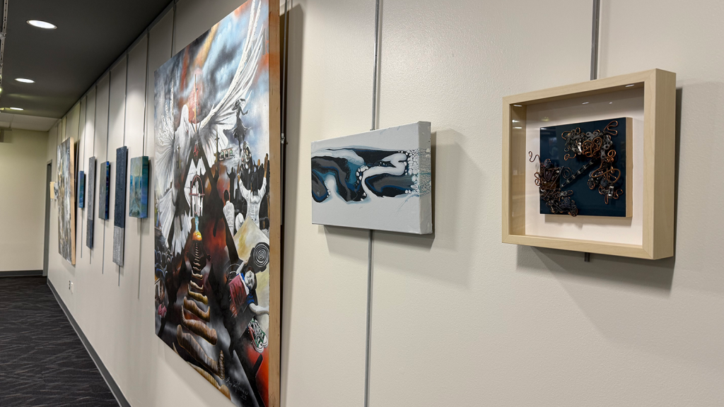 Art paintings of different sizes hang in a row on a wall. Most of the paintings incorporate dark blue colors.