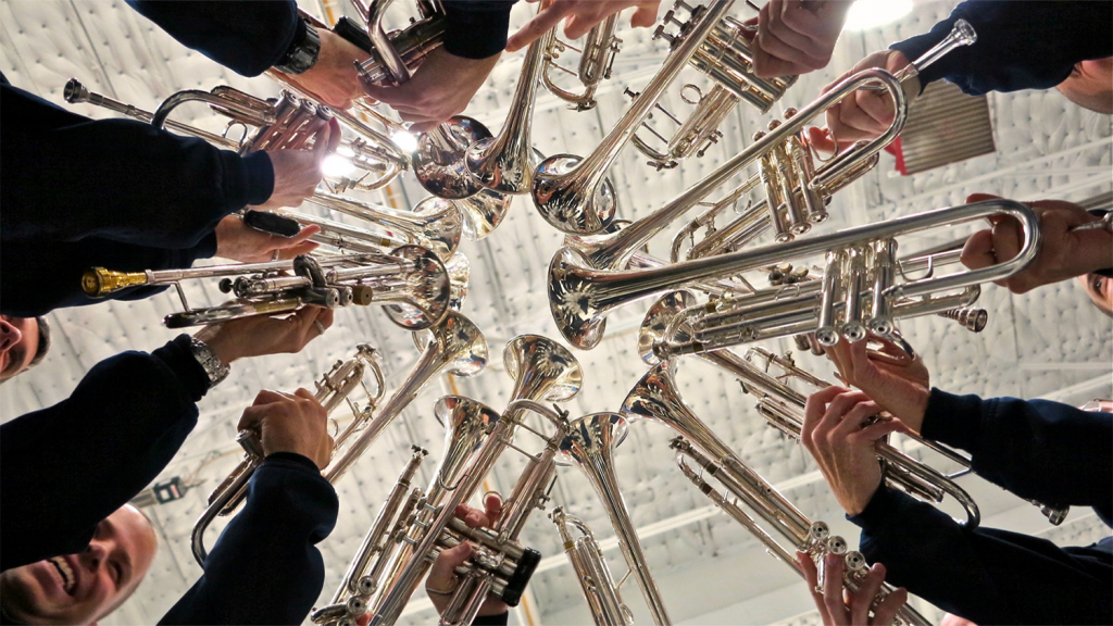 Trumpet players hold their instruments together in a tight circle.