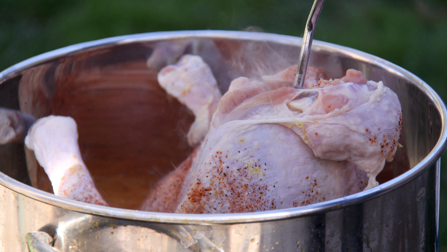 A seasoned chicken smokes in an outdoor fryer.