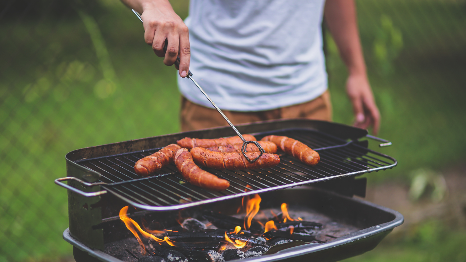 A man grills hot dogs outside over an open flame.