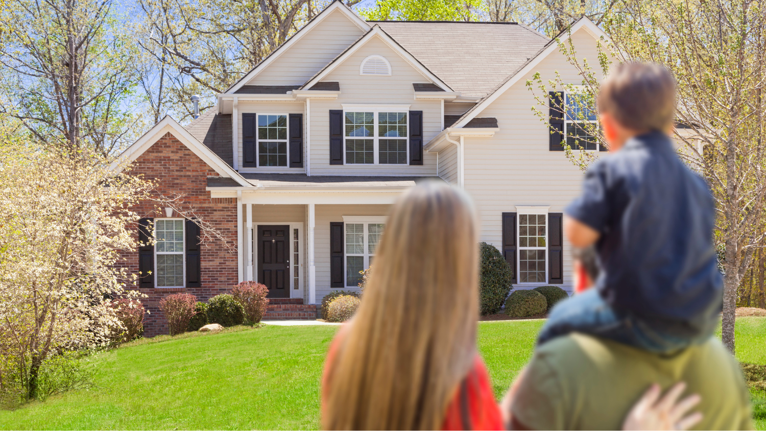 A man, woman and young boy stand looking at a two-story house.
