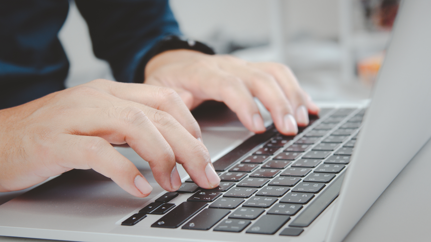 Two hands type on a laptop keyboard.