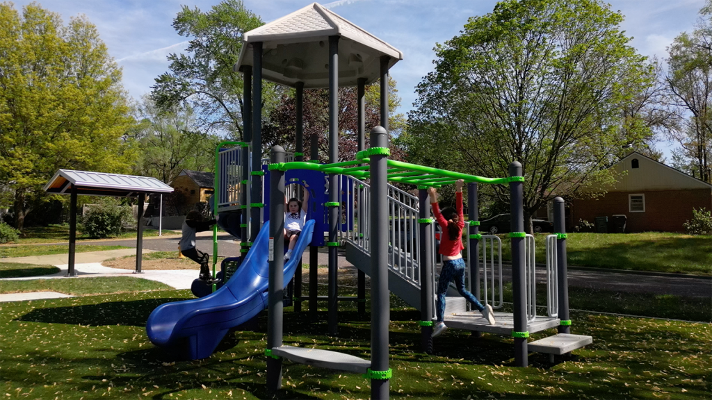 Two young children play on playground equipment, one preparing to go down the slide and the other swinging on the monkey bars.