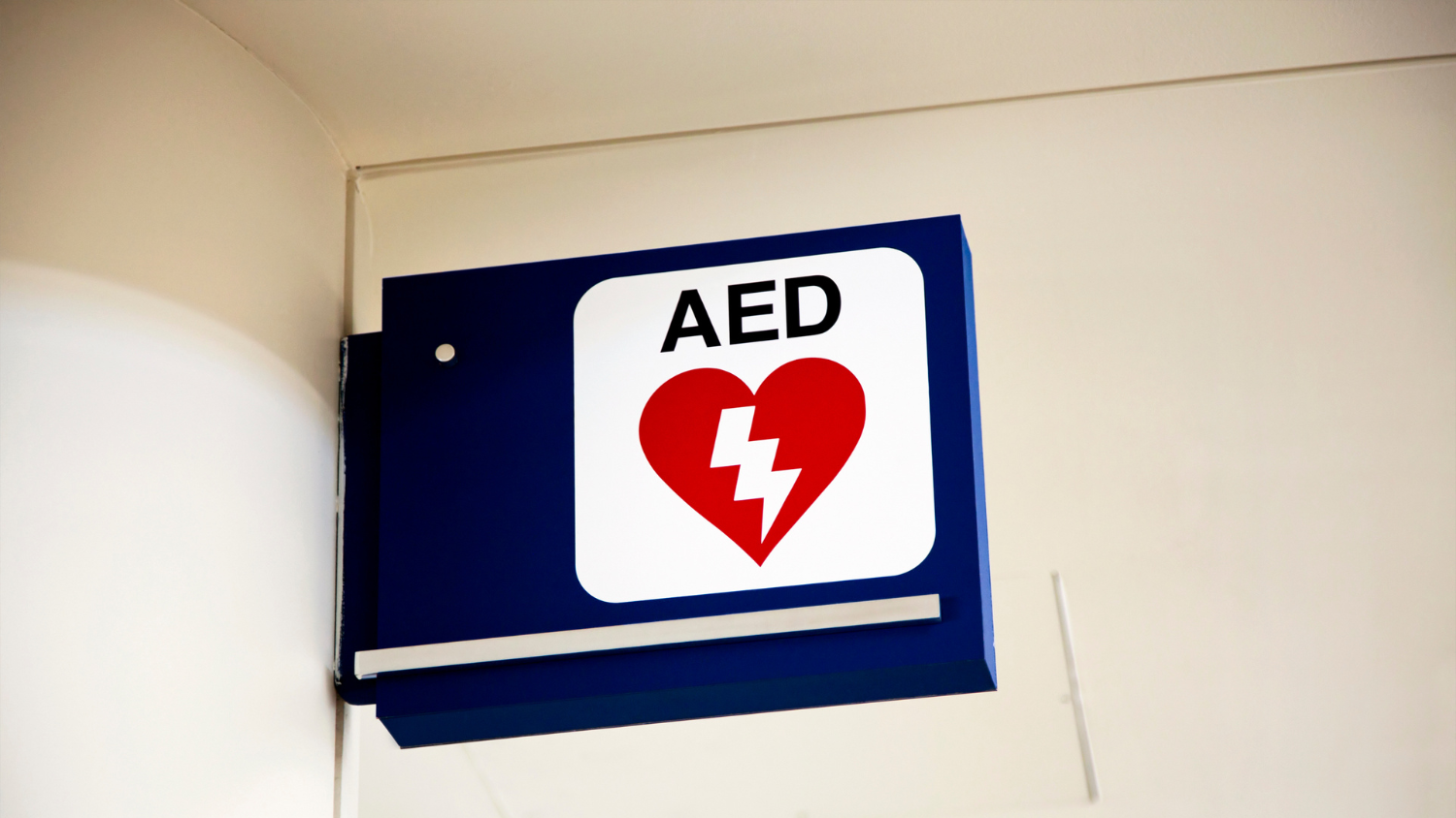 A blue and white sign, which says "AED" and has a heart with a lightning bolt, hangs off a wall.