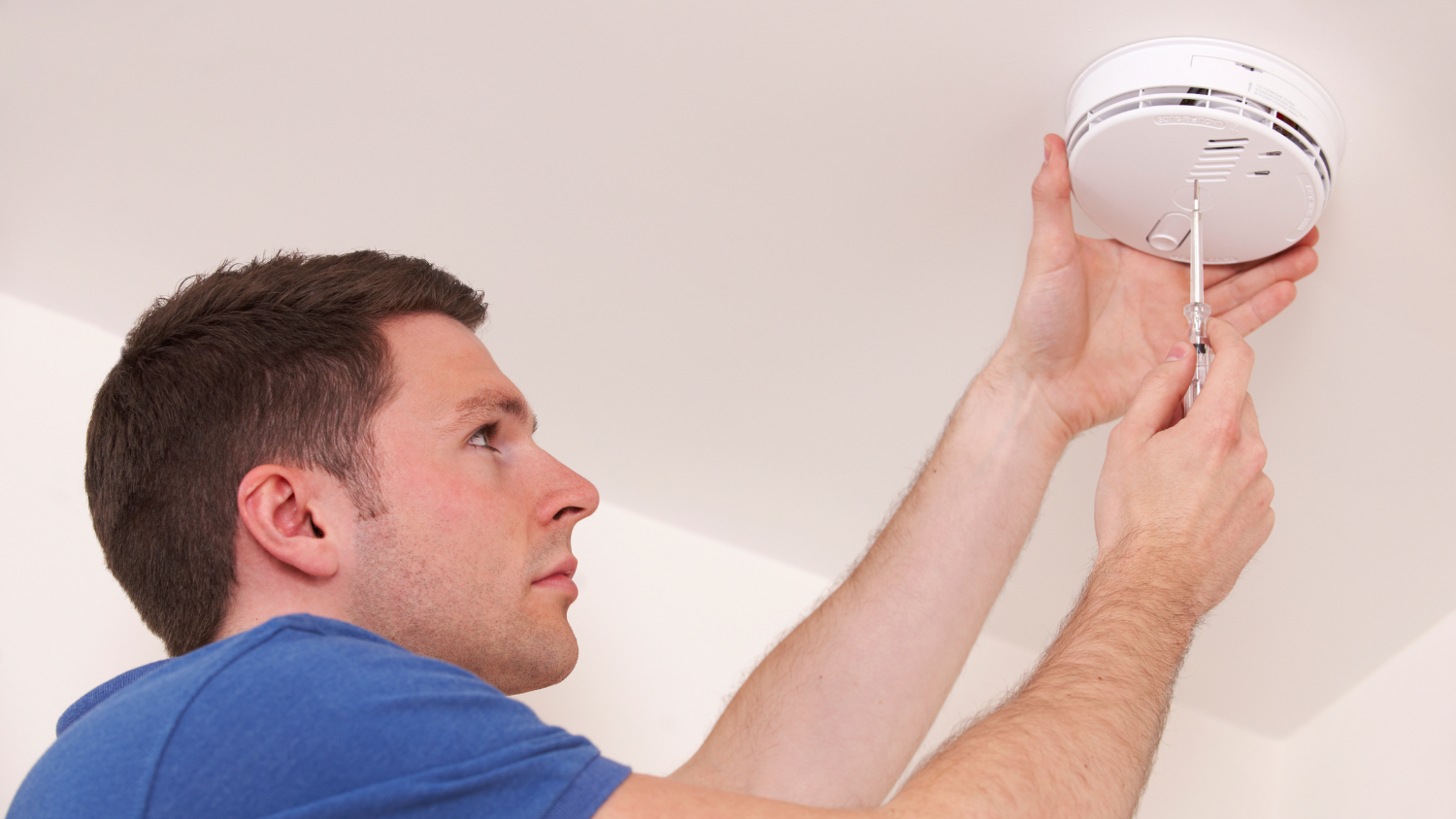 A man uses a screwdriver to secure a fire alarm to the ceiling.