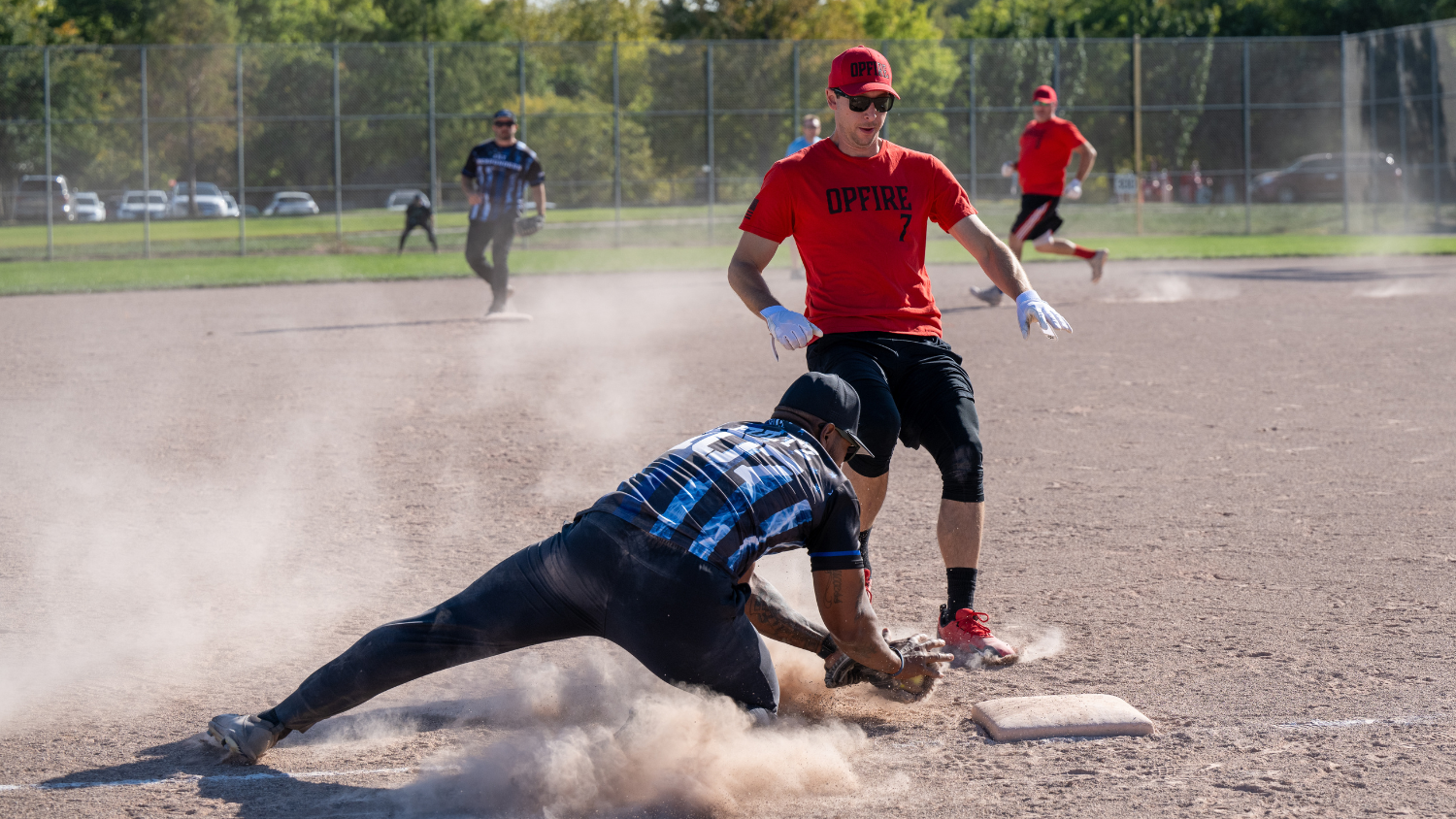 a police officer dives to tag a firefighter on a base in a friendly softball game